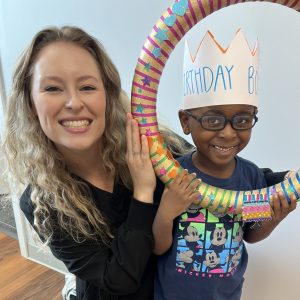 Heather Woodberry, OTR/L with cute pediatric client wearing glasses, a birthday hat and a big smile at Savannah Speech and Hearing Center